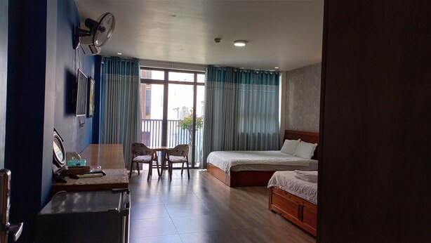 A hotel room with a bed, a desk, a chair, a fan, and a view of the outside. - Capybara Hotel (Ho Chi Minh City)