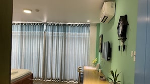 A bedroom with a bed, a desk, a chair, a potted plant, and an air conditioning unit. - Capybara Hotel (Ho Chi Minh City)
