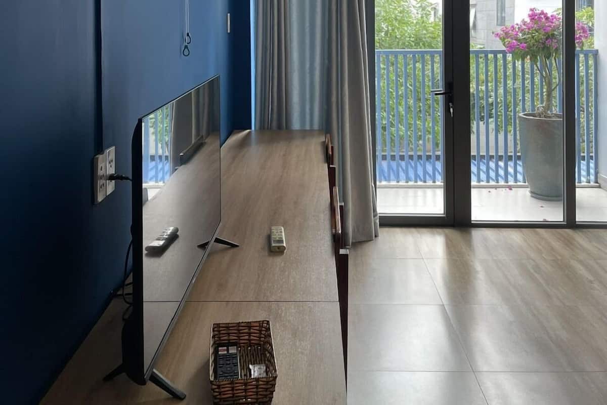 A room with a blue wall, a ceiling fan, a large window with curtains, a wooden table, and a balcony with a potted plant.