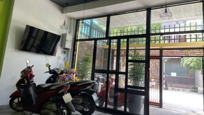 A spacious room with a large sliding glass door leading to an outdoor area, a mounted television on the wall, and a scooter parked inside. - Capybara Hotel (Ho Chi Minh City)
