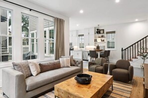 A modern living room with a sofa, armchairs, a coffee table, and a kitchen in the background.
