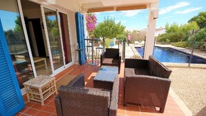 Une terrasse extérieure aménagée avec des meubles en osier, une piscine et une vue sur les environs.
