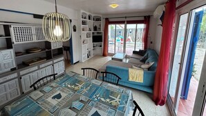 Un salon chaleureux avec un canapé bleu, une table à manger recouverte d’une nappe à motifs et un luminaire suspendu.