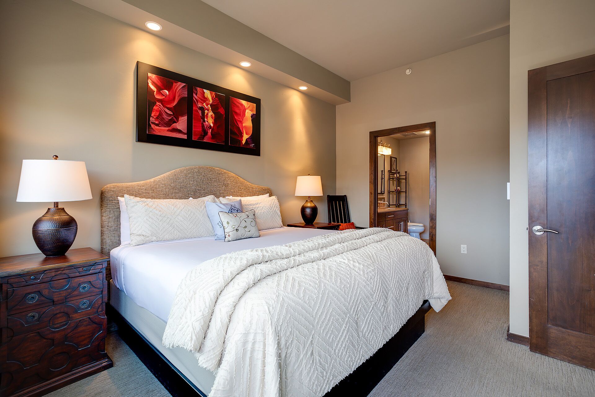 A bedroom with a large bed, two bedside tables with lamps, a decorative mirror, and a painting on the wall.