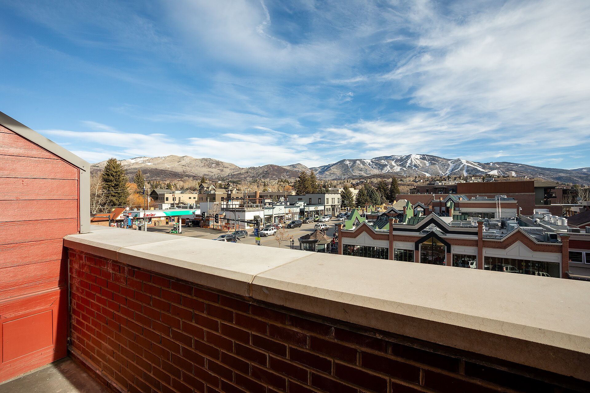 Une vue d'une ville avec une chaîne de montagnes en arrière-plan, un parking et des bâtiments dotés de devantures de magasins.