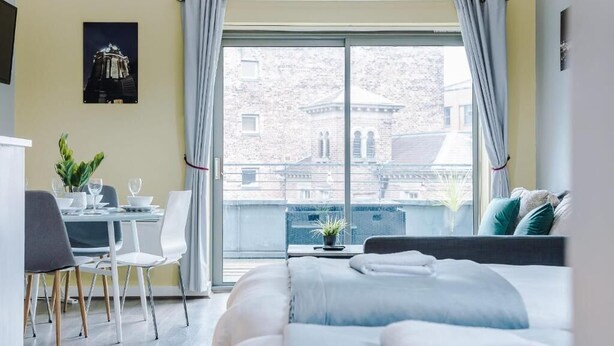 Moderni hotellihuone, jossa on suuri ikkuna, sänky, työpöytä tuolilla ja ruokailutila.