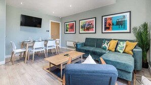 A modern living room with a green sofa, a dining table with chairs, and framed artwork on the wall. - Host & Stay | The Georgian Quarters at Canning III (Liverpool)