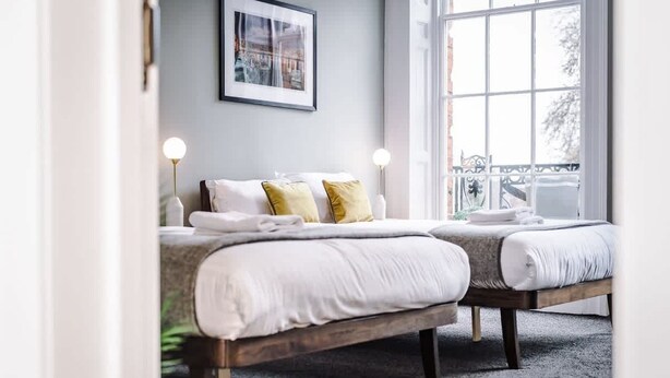 A double bed with white bedding and two pillows, a bedside table with a lamp, and a window with a view of greenery. - Host & Stay | The Georgian Quarters at Canning III (Liverpool)