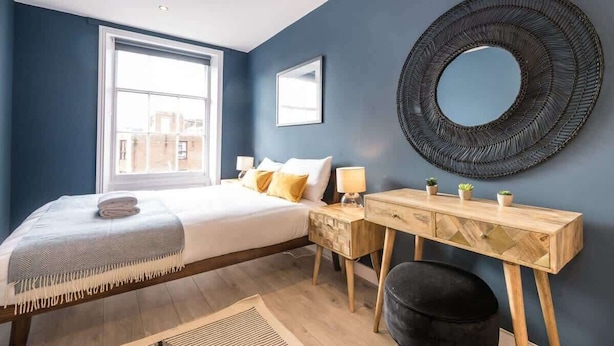 A modern bedroom with a bed, bedside table, and a round mirror on the wall.