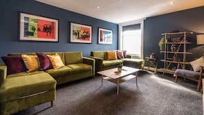 A modern living room with a green sofa set, a coffee table, and a bookshelf.