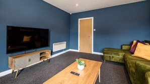 A living room with a large flat-screen TV, a wooden coffee table, a green sofa, and a door.