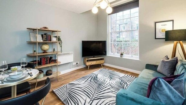 Ett modernt vardagsrum med en soffa, en tv, en bokhylla och en matplats med ett bord dukat för två personer.