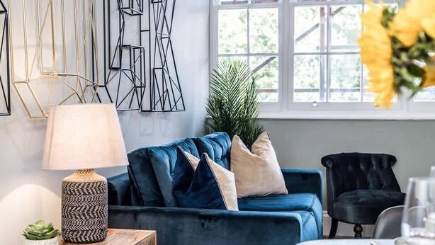 A modern living room with a blue sofa, a black chair, a wooden side table with a lamp, and a dining table set for two. - Host & Stay | Catharine Quarters I (Liverpool)