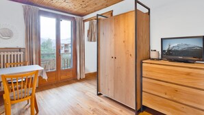 A wooden-paneled room with a dining table, chairs, a TV, and a wardrobe. - Cozy Studio with Wi-Fi, BBQ, Summer Pool, Near Ski Pistes & Free Village Shuttle (Saint-Chaffrey)