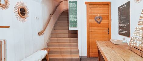 A wooden staircase leading to a room with a heart-shaped decoration on the door, a bench, a table, and a wall with a mirror and a sign.