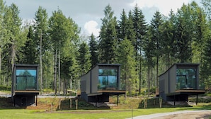 A modern cabin with a glass facade, elevated on stilts, surrounded by a forest. - PihlasResort (Joroinen)