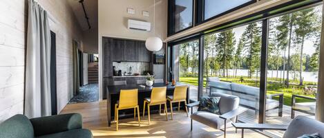 A modern interior with a dining area, kitchen, and large windows offering a view of a landscaped area.
