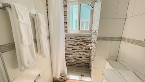 A bathroom with a shower, a toilet, and a window. - Palm Point - 2/2 Townhouse Steps from the Beach (Negril)