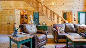 Un vaste salon agrémenté d’un escalier en bois, de meubles en cuir et d’une enseigne indiquant « Noon Beams Cabin Dreams ».