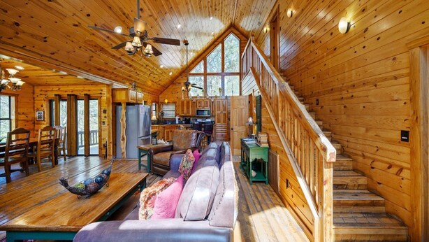 L’intérieur de cette vaste cabane en rondins comprend un coin repas, un salon avec un canapé et un escalier menant à un étage supérieur.
