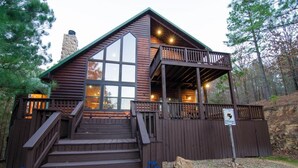 Une cabane avec une façade en bois, une cheminée en pierre, un balcon et une pancarte indiquant qu’il s’agit d’un terrain de camping.