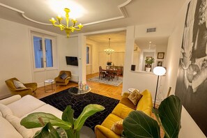 A living room with a sofa, armchair, and a dining area with a chandelier.