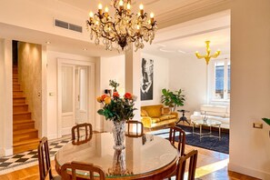 A dining area with a glass table, chairs, a chandelier, and a vase with flowers.