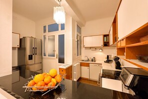 Eine kleine Küche mit Kühlschrank, Herd, Spüle und einer Obstschale auf der Arbeitsfläche.