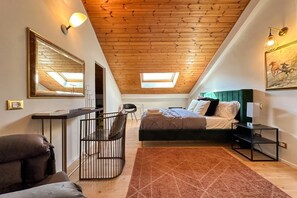 A bedroom with a sloped ceiling, a skylight, a bed, a desk, a chair, and a large mirror.