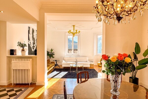A dining area with a table, chairs, a chandelier, and a vase of flowers.