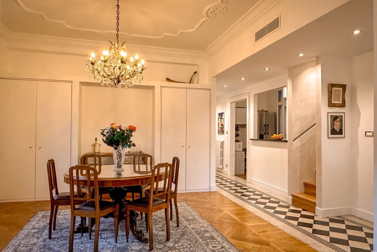 A dining area with a chandelier, a round table, and chairs. There is a patterned rug on the floor.