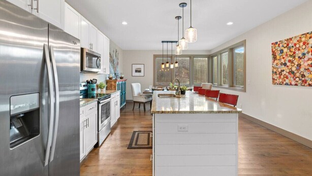 Una cocina moderna con electrodomésticos de acero inoxidable, una isla central, iluminación colgante y un amplio ventanal que proporciona luz natural.