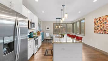 A modern kitchen with stainless steel appliances, a central island, pendant lighting, and a large window providing natural light.