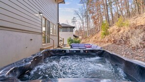 Un jacuzzi frente a una casa con patio y vista a árboles.