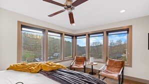 Un dormitorio con una cama grande, ventilador de techo y varias ventanas que dan al exterior.
