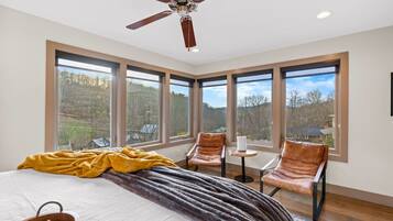 A bedroom with a large bed, a ceiling fan, and multiple windows offering a view of the outdoors.