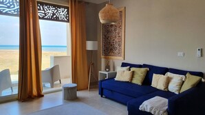 A living room with a blue sofa, a small side table, a lamp, and a view of the beach. - El Gouna - Sea view - Kitesurfing  (Hurghada)