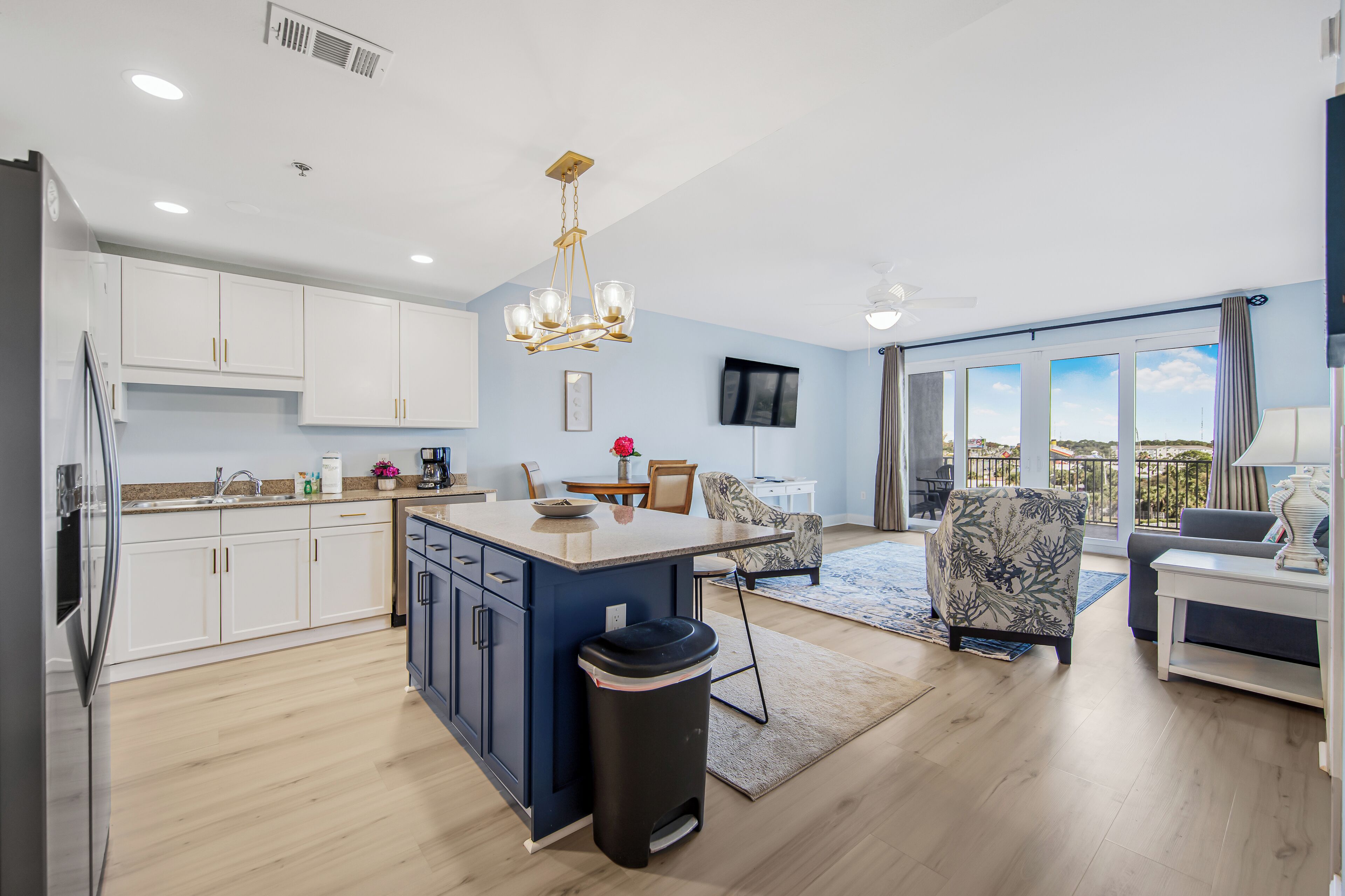 A modern kitchen with white cabinets, a central island, and a black trash bin.