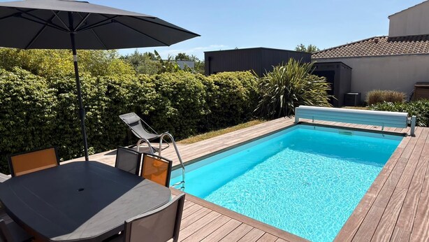 Ein rechteckiger Swimmingpool mit Holzterrasse, Liegestuhl und Tisch mit Sonnenschirm.