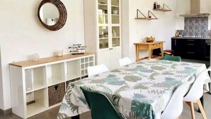 Ein Zimmer mit Esstisch, Stühlen, einem Schrank, einem Spiegel und einer Küchenzeile.