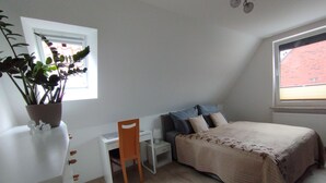 Un dormitorio con cama, escritorio, silla, planta en maceta y ventana.