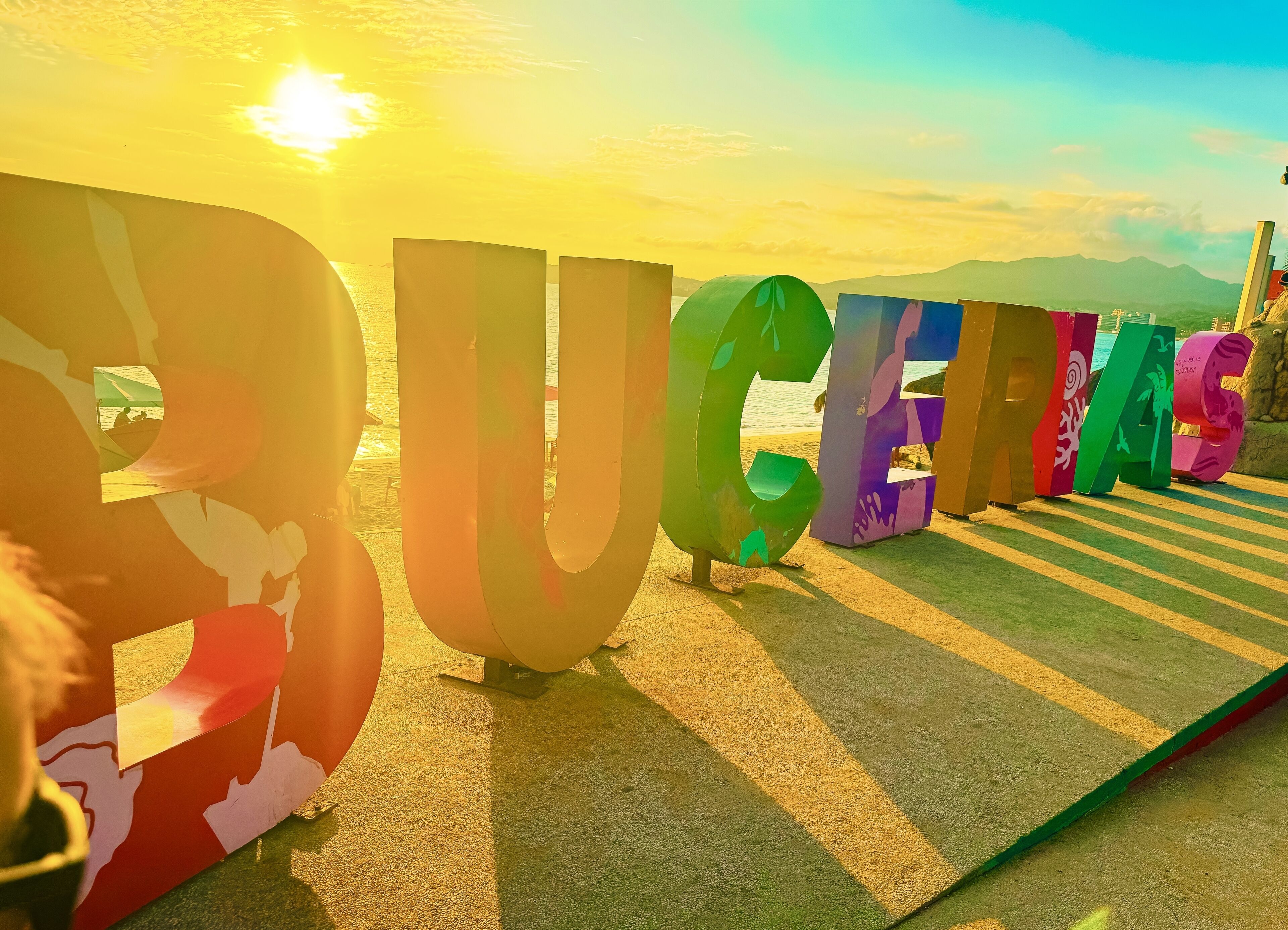 Large, colorful letters spelling "DUCHESS" on a beach with a sunset in the background.