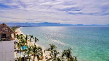 Una playa con agua turquesa cristalina, palmeras y un edificio con techo de paja.