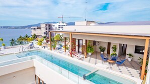 A rooftop pool with clear blue water, surrounded by lounge chairs and potted plants. - Casa Kaia, Ocean-View Boho-Chic, 2bd/2ba Condo in Golden Zone (Bucerías)