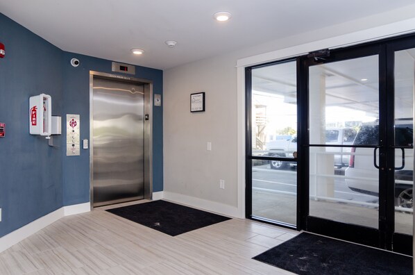 A hotel lobby with a blue wall, an elevator, a fire extinguisher, and a glass door leading outside. - A Wish Granted: End unit in Carolina Surf (Carolina Beach)