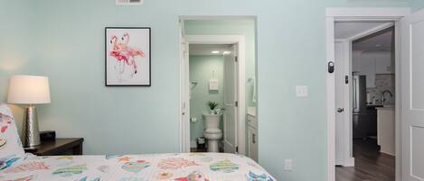 Een slaapkamer met een bed, een nachtkastje, een wandlamp en een lijst met flamingo’s.