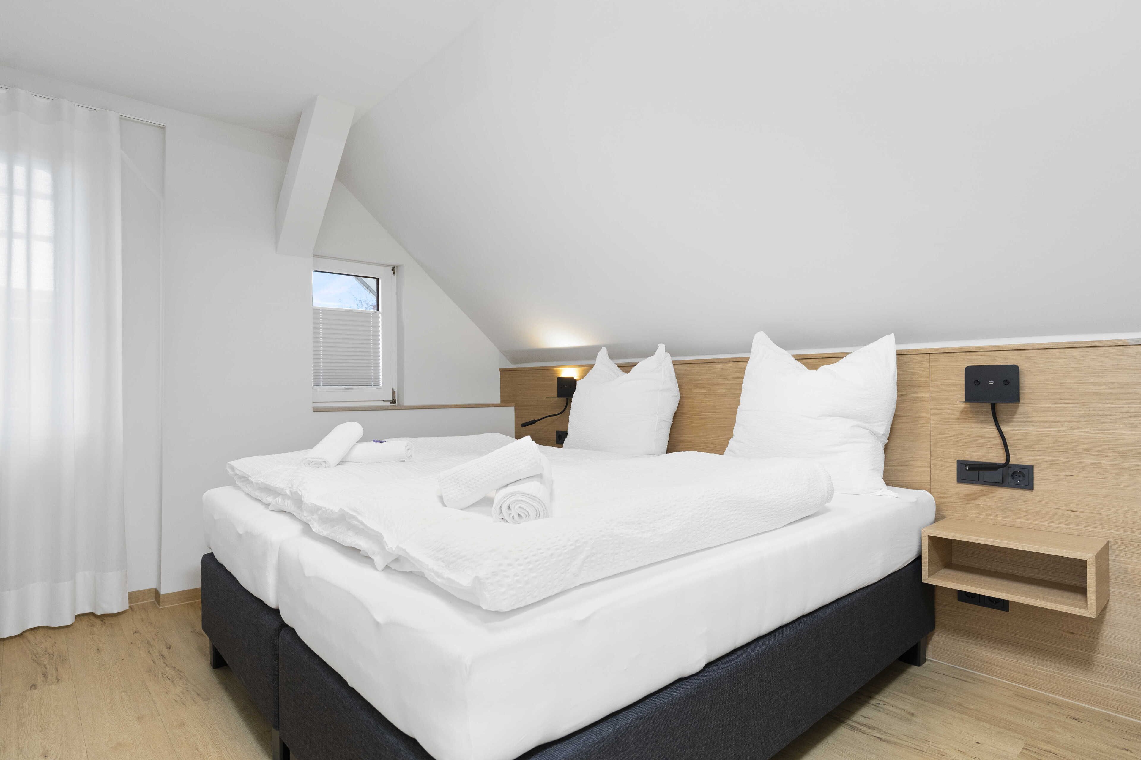 Ein modernes Schlafzimmer mit einem großen Bett, weißen Leinen, einem Holzkopfende und einem Nachttisch.