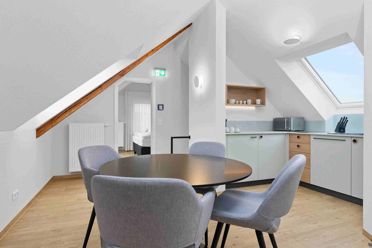 A modern kitchen with a skylight, a dining area with a round table and four chairs, and a visible staircase leading to another room.