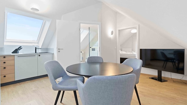 A modern kitchen with a skylight, a dining area with a round table and four chairs, and a large flat-screen TV. - Hotel Garni Traube (Friedrichshafen)
