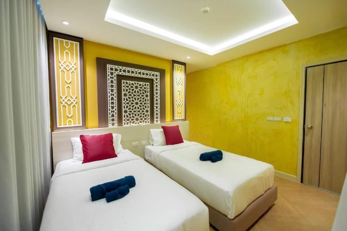 A hotel room with two beds, a skylight, decorative wall panels, and a wooden wardrobe.